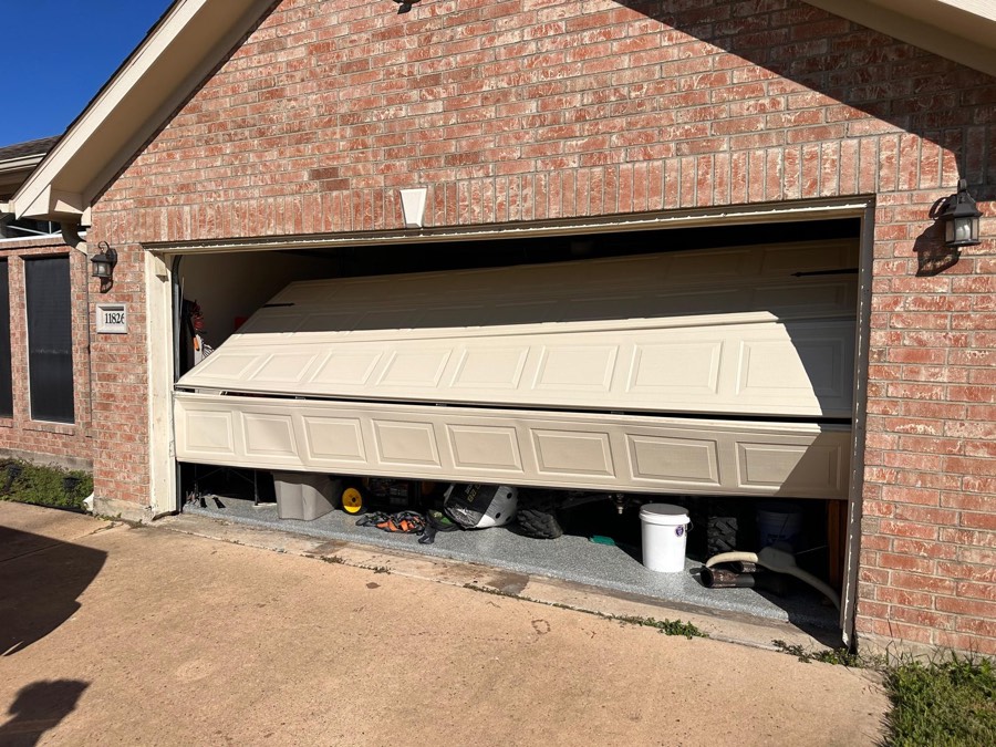 Garage door hanging crooked off its track on a brick home