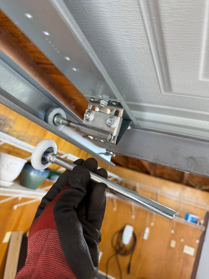 Technician's gloved hand servicing garage door rollers and track